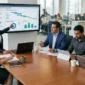A diverse team of SAP consultants and business professionals collaborating around a conference table in a modern office while reviewing S/4HANA digital transformation analytics on large monitors.