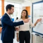 Two professionals point to a whiteboard process diagram during a business strategy session.