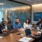Diverse professionals sitting around a conference table with laptops, viewing global network overlays and data dashboards.